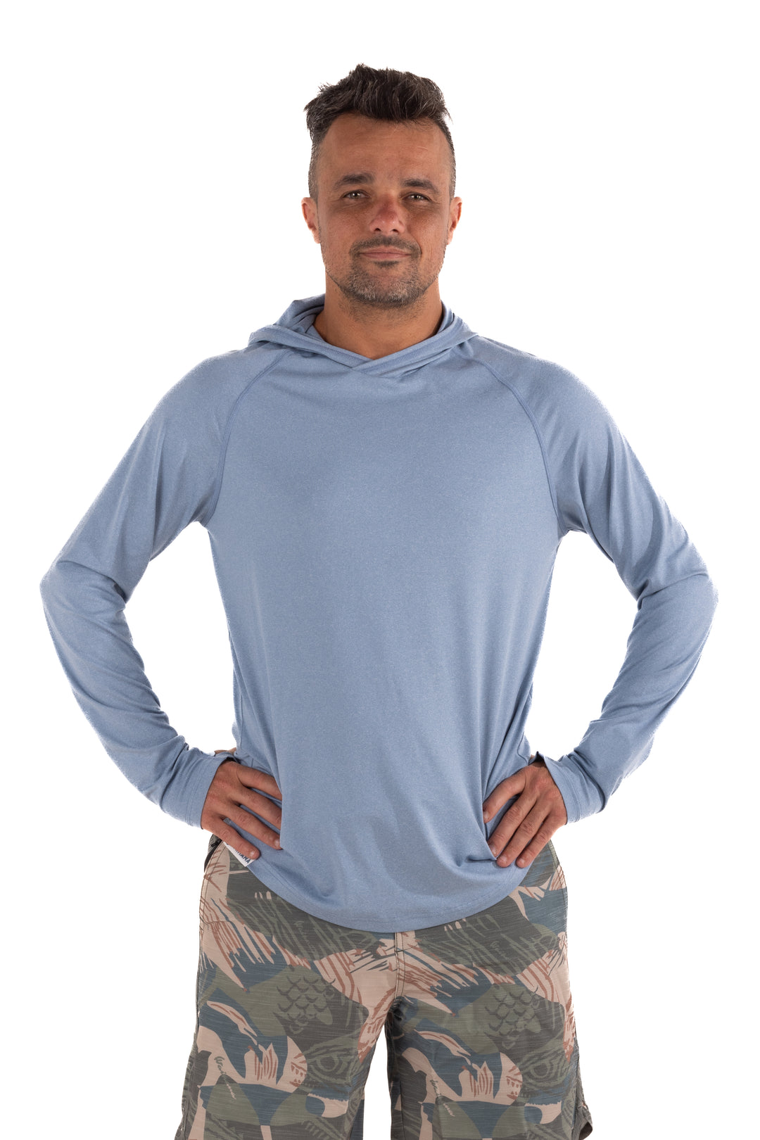 Male model wearing the Waihana Mariner Blue Hooded Long Sleeve sun shirt in light blue with raglan sleeves, paired with tropical-print board shorts, on a white background.