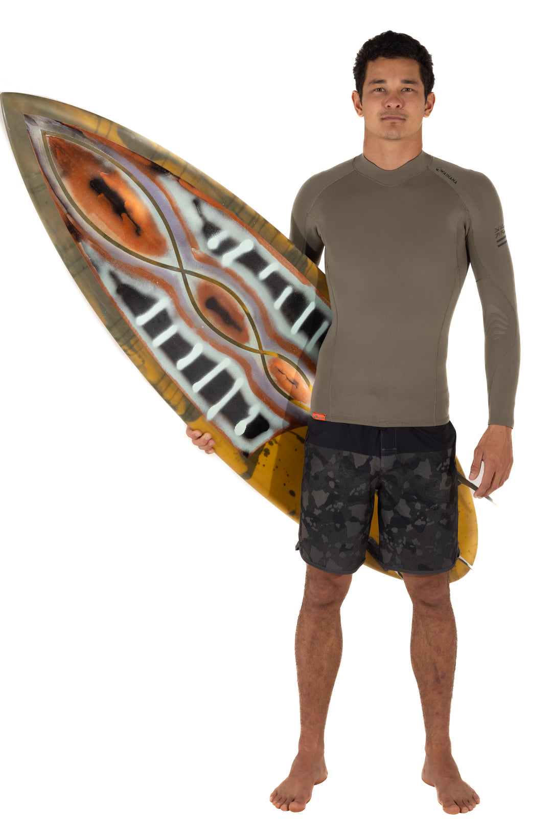 Male model wearing a Waihana Ranger Green long-sleeve surf rashguard top paired with dark camo board shorts, holding an artistically painted surfboard against a white studio background.